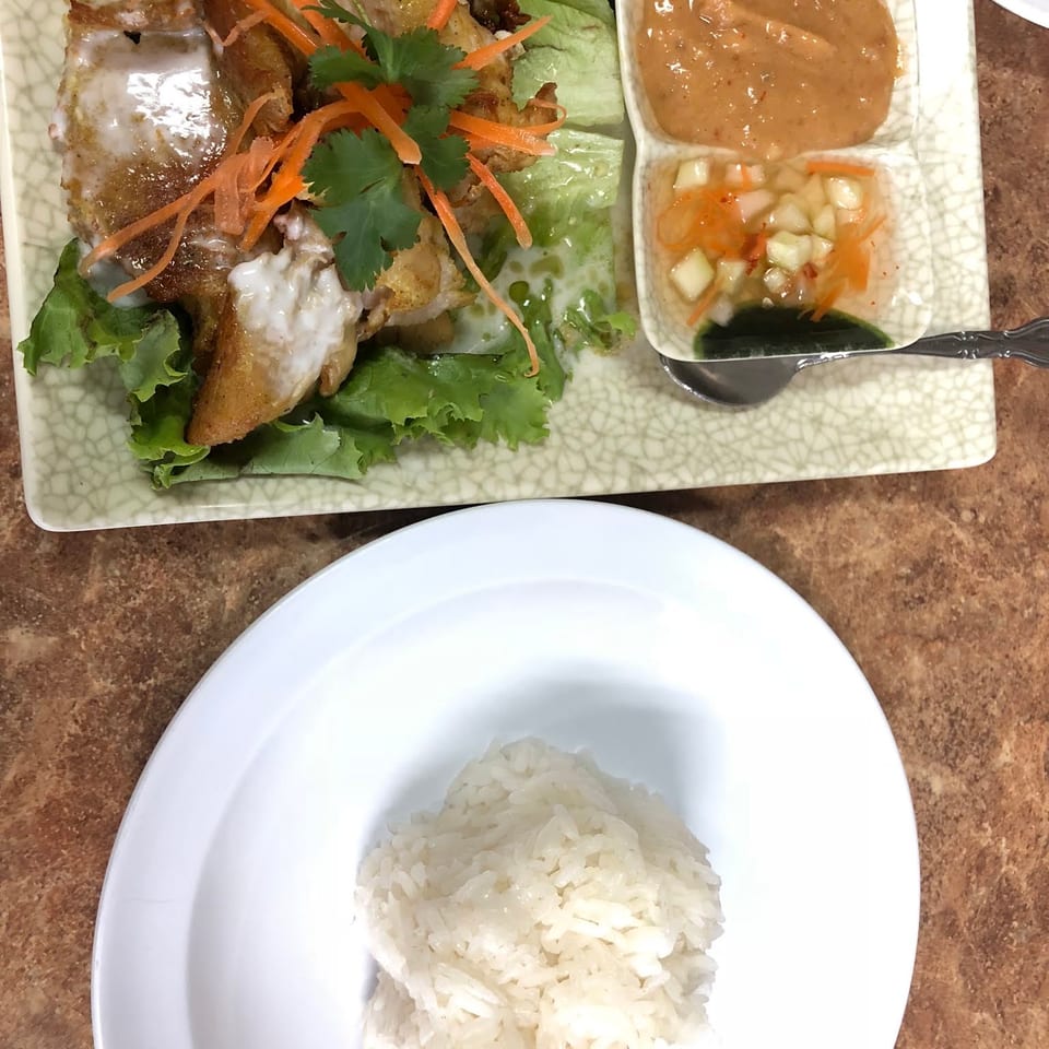 Crispy chicken with lettuce, shredded carrots, cilantro, peanut sauce, and pickled vegetables, served with white rice.