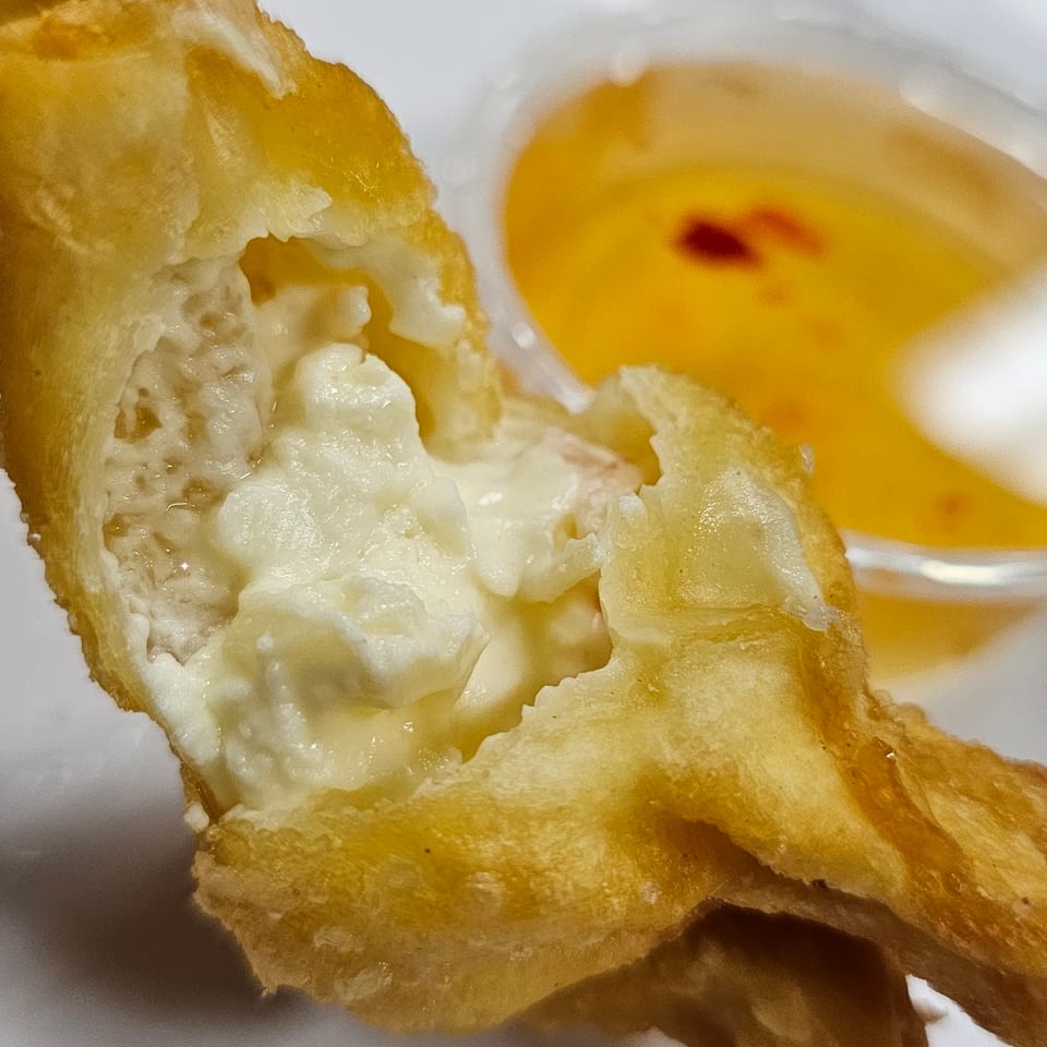 A close-up of a crab rangoon, split open to reveal its creamy white filling, with dipping sauce.