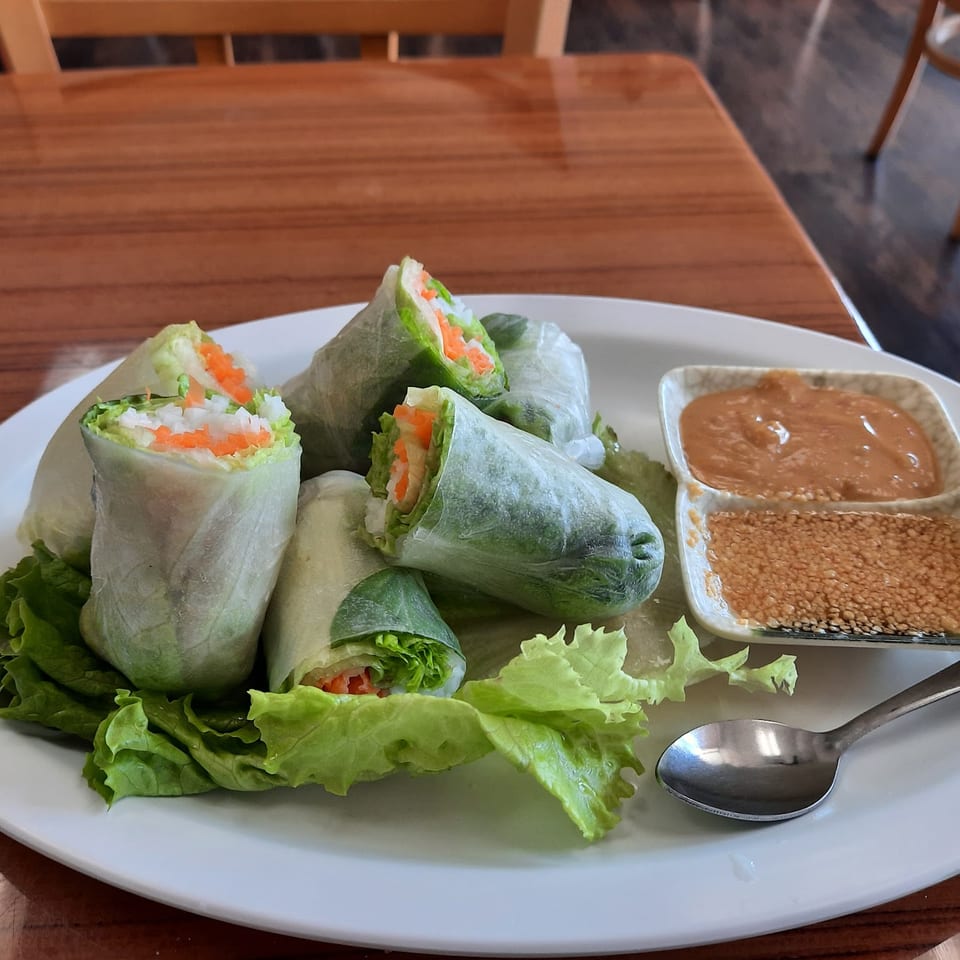 Fresh spring rolls with lettuce, carrots, and rice noodles, served with peanut sauce and sesame seeds.