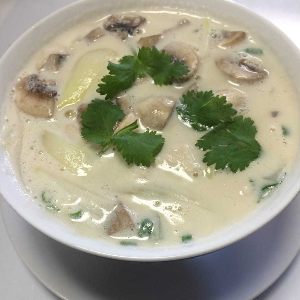 Creamy white soup with mushrooms, onions, and cilantro in a white bowl on a white plate.